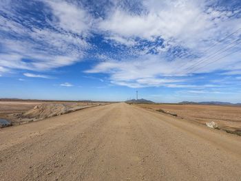 Dirt road amidst landscape against sky