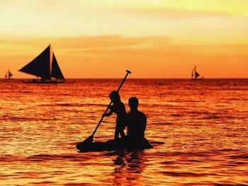 Silhouette men in sea against sky during sunset