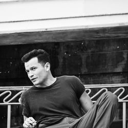 Portrait of young man looking away while sitting on window