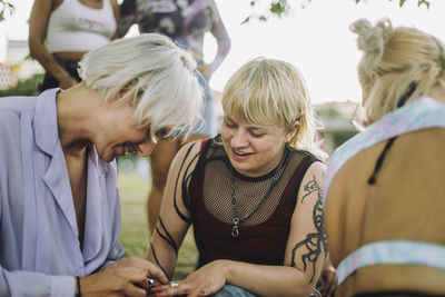 Smiling non-binary person applying nail polish to friend sitting by woman