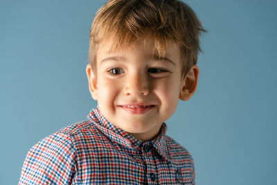 Close-up of smiling boy looking away against blue background