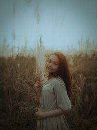 Young woman standing on field against sky