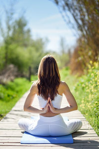 Full length of woman doing yoga on boardwalk against plants