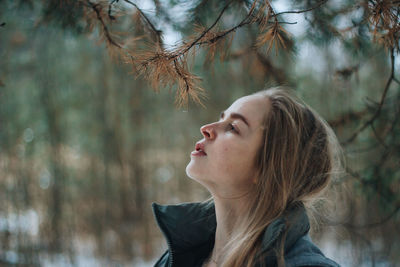 Close-up of young woman looking up at branch