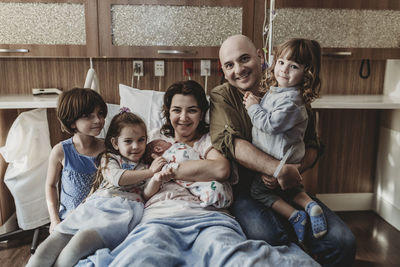 Mid view of whole family holding newborn son and smiling in hospital