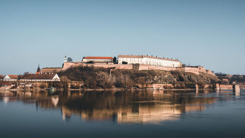 Buildings by lake against clear blue sky