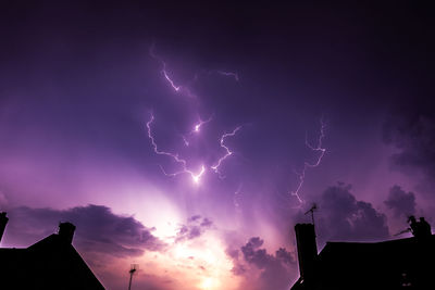 Low angle view of lightning over silhouette buildings against sky