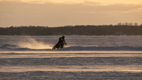 Motocrosso on frozen lake against sky during sunset