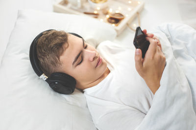 Teenager boy using mobile phone while lying on bed