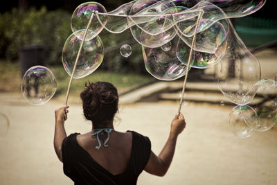 Rear view of woman making large bubbles on street