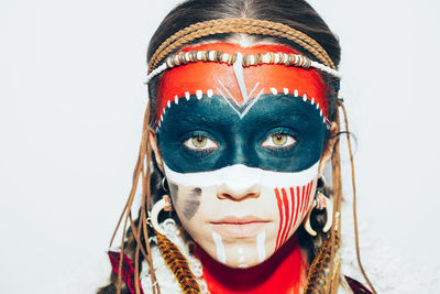 Close-up portrait of woman with face paint looking away against white background