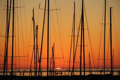 Silhouette sailboats on sea against orange sky