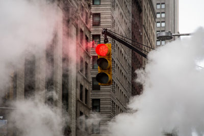 Low angle view of illuminated stoplight amidst smoke in city