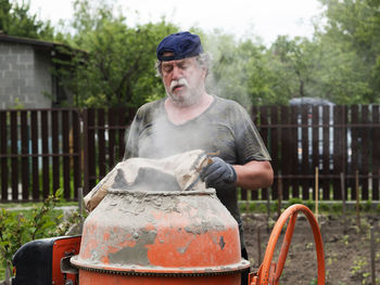 Mature caucasian man pours cement from a bag into a concrete mixer