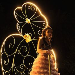 Portrait of young woman standing against illuminated lighting equipment