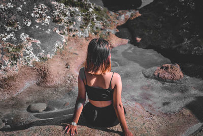 Rear view of woman sitting on rock