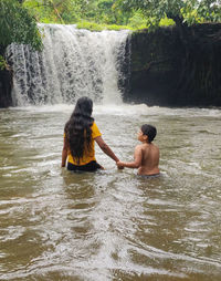 Rear view of woman standing in waterfall