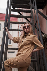 Three quarter length outside portrait of a fashion model in sunglasses and beige suit in urban area