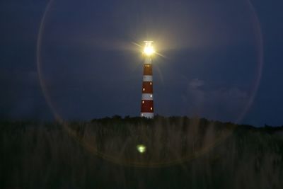 Illuminated road sign on field against sky at night