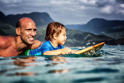 Father and 3 year old sun paddling on a wooden surfboard