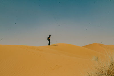 Man on sand dune in desert against sky