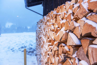 Full-sized side view of freshly beaten, stacked on a barn and snow-covered firewood in snowfall.