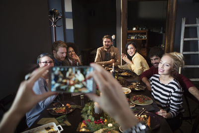 Cropped image of woman photographing happy friends while enjoying meal