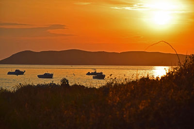 Silhouette boats in lake against orange sky