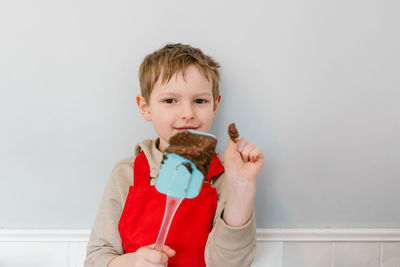 Portrait of cute boy holding camera while standing against wall