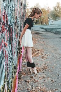 Side view of young woman dancing on road by wall