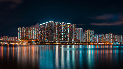 Illuminated buildings by sea against sky at night