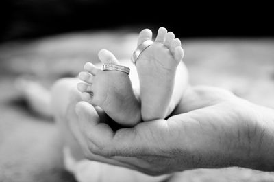 Cropped hand of father holding baby girl feet with rings at home