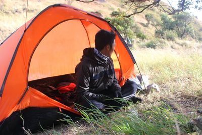 Rear view of man sitting in tent on field