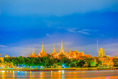 Illuminated building by lake against blue sky