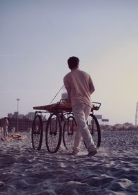 Rear view full length of vendor with cart at sandy beach against sky