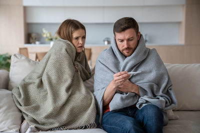 Family couple young man woman measuring temperature sitting on couch wrapping in plaids.