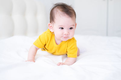 Healthy asian baby girl 5 months in yellow bodysuit on bed on white bedding