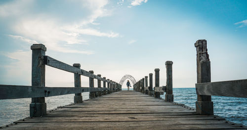 Full length of woman standing on wooden pier by sea against sky