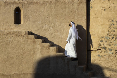 Rear view of woman walking on wall by building