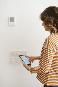 Young woman touching switch for blinds while checking mobile phone app