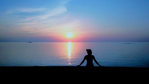 Silhouette man standing in sea against sky during sunset