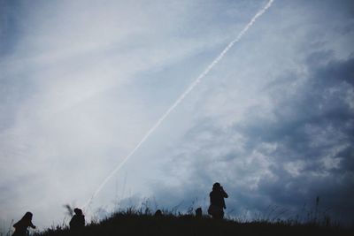 Silhouette people standing on field against vapor trail in sky