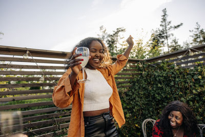 Carefree young woman dancing while holding drink glass during dinner party