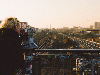 Side view of woman looking in coin-operated binoculars at railroad tracks