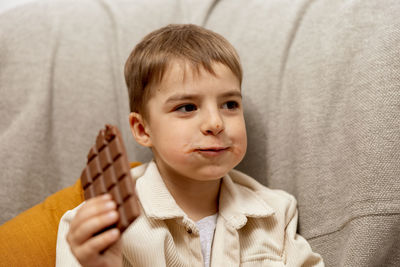 Little adorable boy sitting on the couch at home and eating chocolate bar. child and sweets