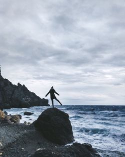 Woman standing on rock at beach against sky