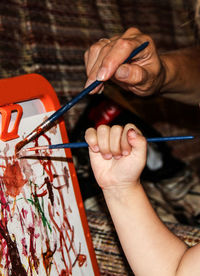 Cropped hands of father and child painting on paper