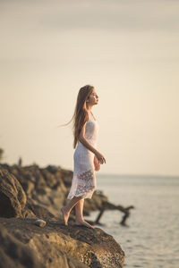 Woman on rock at beach against sky during sunset