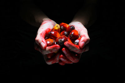 Close-up of hand holding strawberry over black background