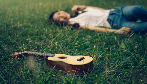 Smiling young woman listening music by ukulele on grass